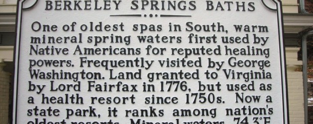 A historical marker titled "Berkeley Springs Baths" explains that it is one of the oldest spas in the South, with warm mineral springs first used by Native Americans. Frequently visited by George Washington, it has been a health resort since the 1750s and is now a state park.
