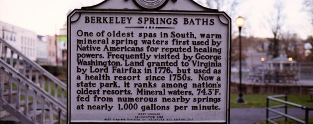 A historical marker titled "Berkeley Springs Baths" describes the site as one of the oldest spas in the South, with warm mineral spring waters historically used by Native Americans and notable figures like George Washington. The springs feed nearly 1,000 gallons per minute.