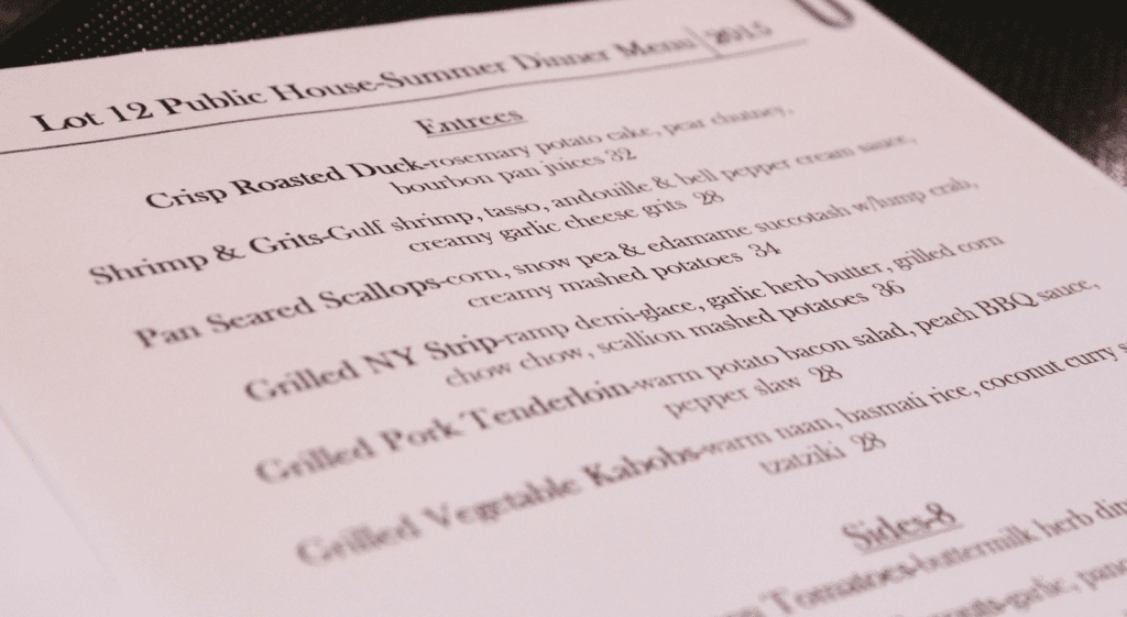 Menu titled "Lot 12 Public House: Summer Dinner Menu 2015." It lists entrees that include Crisp Roasted Duck, Shrimp & Grits, Pan-Seared Scallops, Grilled NY Strip, Grilled Pork Tenderloin, and Grilled Vegetable Kabobs. A section titled "Sides" is partly visible.