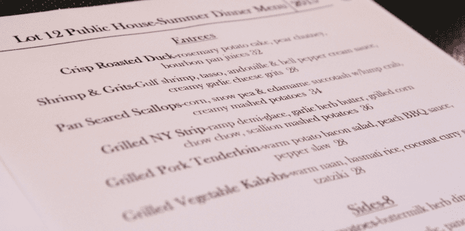 Menu titled "Lot 12 Public House: Summer Dinner Menu 2015." It lists entrees that include Crisp Roasted Duck, Shrimp & Grits, Pan-Seared Scallops, Grilled NY Strip, Grilled Pork Tenderloin, and Grilled Vegetable Kabobs. A section titled "Sides" is partly visible.
