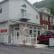 A two-story building with a stone facade on the lower level and white siding on the upper level. The building features arched windows and a small balcony. A red SUV is parked in front, and a sign reads "Maria's Garden & Inn Bed & Breakfast, Bakery, Restaurant.