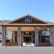 The image shows the front entrance of a Best Western hotel. The building features a wooden facade with stone pillars supporting a large overhang. The Best Western sign is prominently displayed above the entrance. An American flag is visible to the right of the entrance.