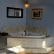 A tiled corner bathtub with a central faucet in a blue-walled room. A basket sits on the ledge beside the tub, and a small candle is on the other side. A mirror is mounted above the tub, and a framed painting hangs on the adjacent wall.
