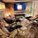 Three people relax in recliner chairs in a dimly lit room, simulating a cave-like environment with textured walls. They are watching a screen displaying a warm, glowing image. A modern electric fireplace adds to the cozy ambiance.